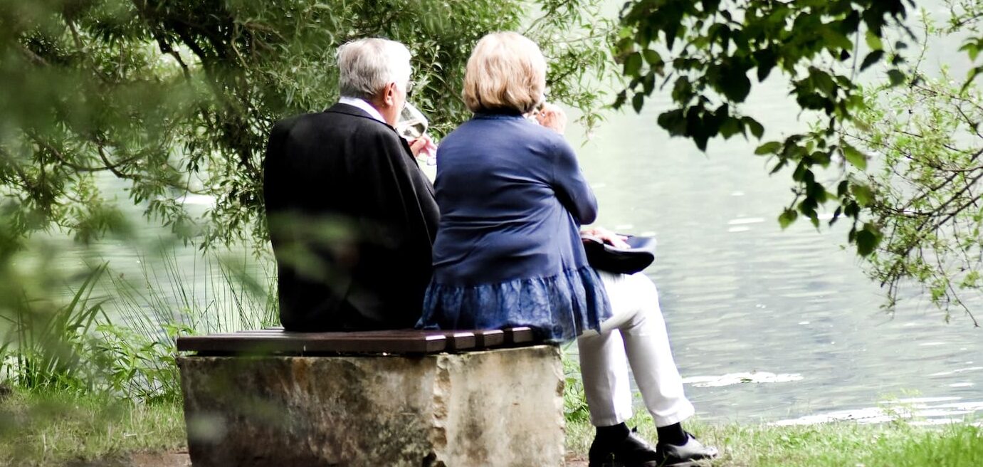 two people sitting on pavement facing on body of water